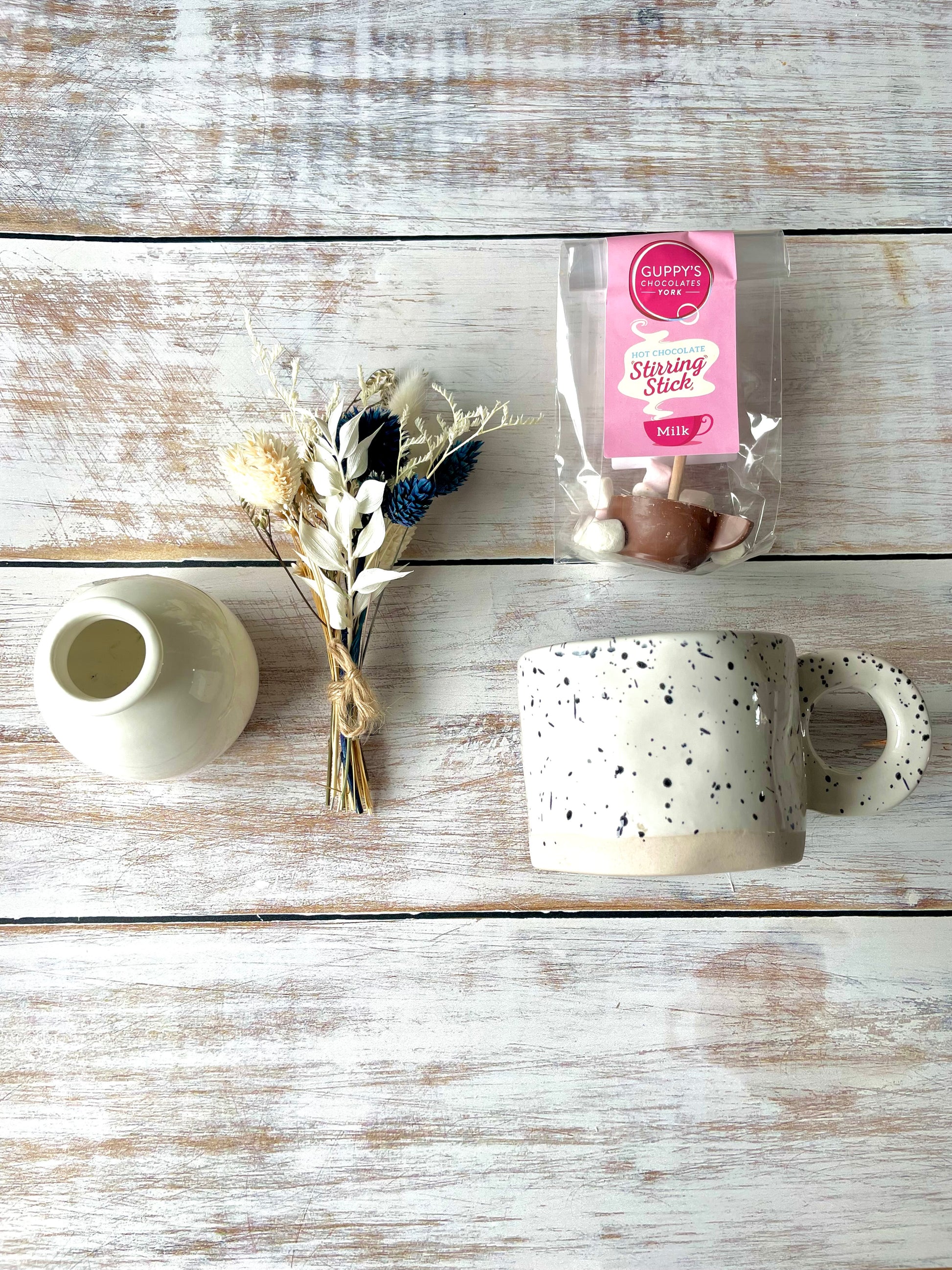 Ceramic mug with speckled pattern, small vase, bouquet of dried flowers, and a hot chocolate stirrer